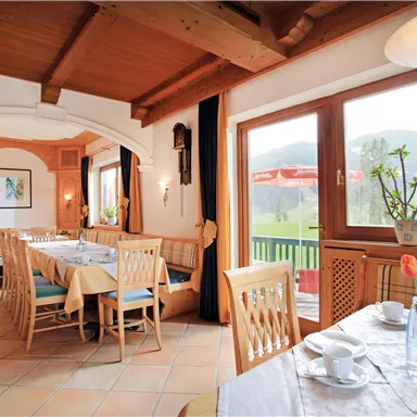 Ein gemütliches Restaurant mit Holzdecke und großen Fenstern. Tische sind gedeckt und bieten einen Blick auf die grüne Landschaft draußen.