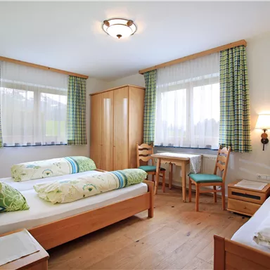 Ein helles Zimmer mit zwei Einzelbetten und einem Schreibtisch. Die großen Fenster bieten viel Tageslicht und Blick auf die Umgebung.