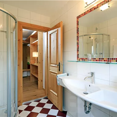 Ein modernes Badezimmer mit einer Dusche, einem Waschbecken und Holzelementen. Der Boden ist mit rot-weißen Fliesen gestaltet.