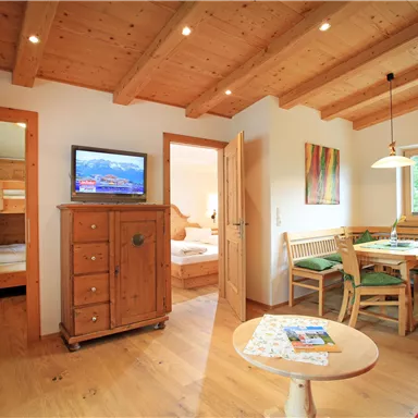 Ein gemütlicher Wohnraum mit Holzdecken und modernen Möbeln. Es gibt einen Tisch, Stühle und einen Fernseher in der Mitte des Raumes.