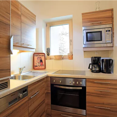 Eine moderne Küche mit Holzschränken und weißen Arbeitsflächen. Sie verfügt über Geräte wie einen Herd, einen Mikrowellenofen und eine Kaffeemaschine.