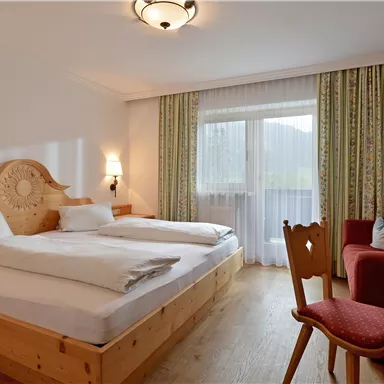 Ein gemütliches Hotelzimmer mit Holz-Möbeln und einem Doppelbett. Es gibt einen kleinen Tisch, einen Fernseher und Zugang zu einem Balkon mit Blick nach draußen.