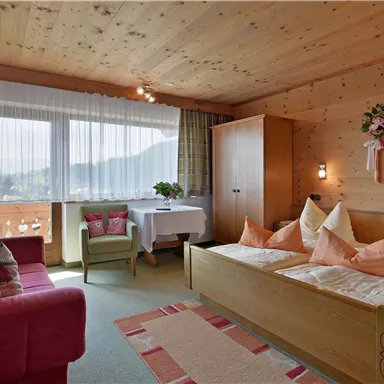 A cozy room with wooden walls, a double bed, and a red sofa. Large windows provide a view of the landscape.