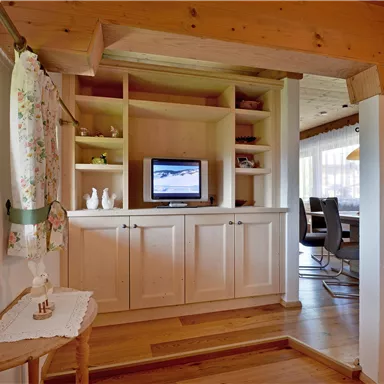 A cozy living space with a wooden shelf, a television, and decorative elements. The room has a warm, inviting character.