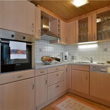 A modern kitchen with light wood cabinets and stainless steel appliances. It is well-equipped with a stove, a sink, and personal decorations.
