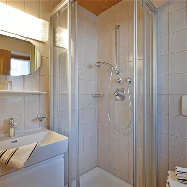 A modern bathroom with a shower, sink, and mirror. The walls are tiled in light colors, and fresh towels are ready.