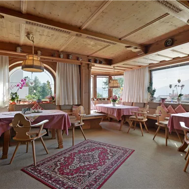 A cozy dining room with wooden walls and colorful tablecloths.
Large windows let in plenty of daylight, and plants create an inviting atmosphere.