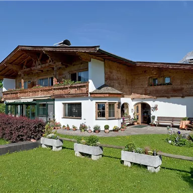 A traditional alpine house with wooden cladding and a beautiful garden. The mountains are visible in the background.