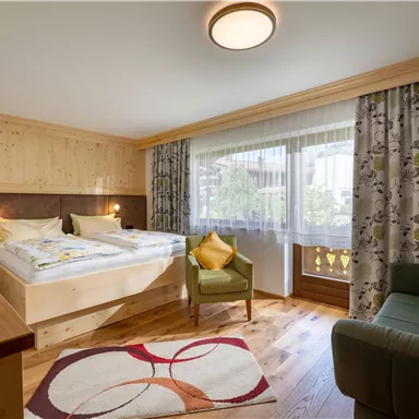 A cozy room with two beds and a small seating area. Large windows allow plenty of light in and the decoration is modern and inviting.