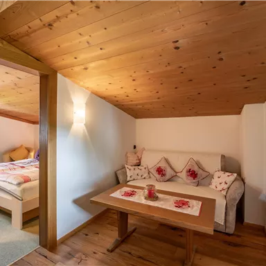 A cozy seating area with a table and a couch in a wood-decor room. In the background, a bedroom is visible.