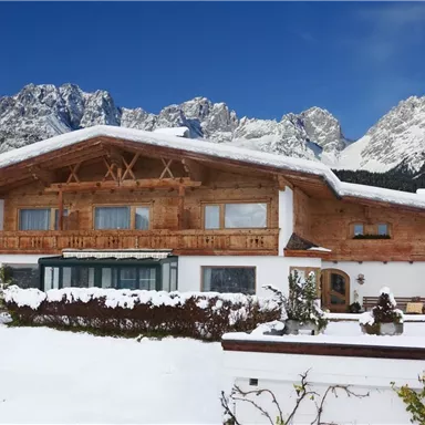 A beautiful chalet in the snow, surrounded by majestic mountains. The clear blue sky gives the winter landscape a serene atmosphere.