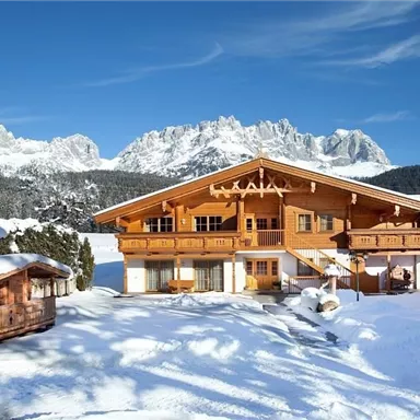 Ein wunderschönes Holzhaus im Winter, umgeben von Schnee und Bergen. Der klare blaue Himmel sorgt für eine idyllische Atmosphäre.