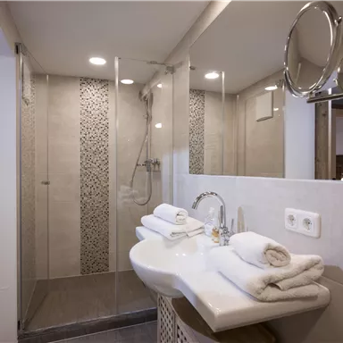 A modern bathroom with a glass shower and elegant tiles. Fresh towels are laid out on the sink.