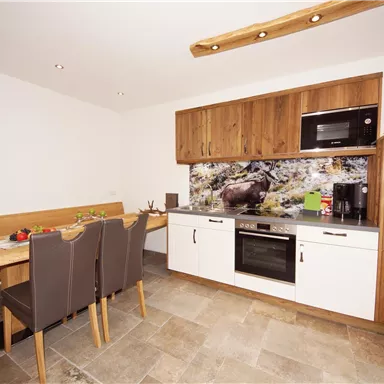 Eine moderne Küche mit Holzschränken und einer gemütlichen Essecke. Die Wände sind hell und die Ausstattung ist modern und funktional.