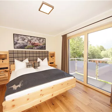 Ein gemütliches Schlafzimmer mit einem großen Bett und Holzmöbeln. Von den Fenstern aus hat man einen Blick ins Grüne.