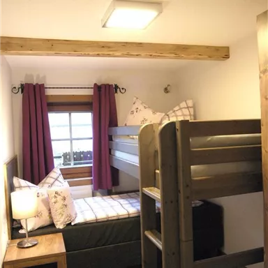 A cozy room with a bunk bed and a single bed. Large windows let in plenty of light and the curtains provide privacy.