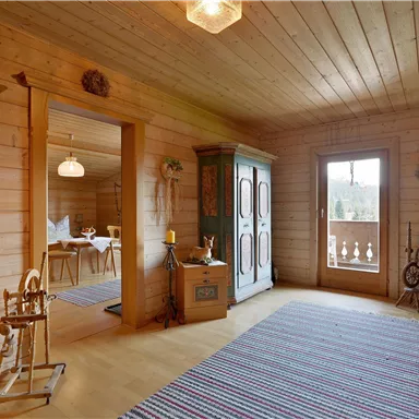 A cozy room with wooden walls and a colorful carpet. In the background, a beautiful view can be seen through a window.