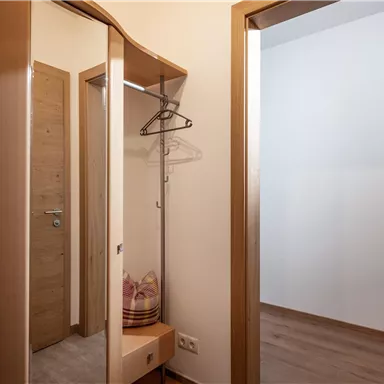 A bright hallway with a mirror and a coat rack. The walls are neutral and the floor is made of wood.
