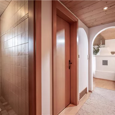 Ein einladender Eingangsbereich mit einem Badezimmer auf der linken Seite und einem gemütlichen Wohnraum auf der rechten Seite. Die Holzverkleidung und der Teppich sorgen für eine warme Atmosphäre.