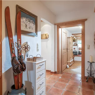 A cozy hallway with wooden details and ski equipment on the wall. The room has terracotta-colored tiles and plenty of natural light.
