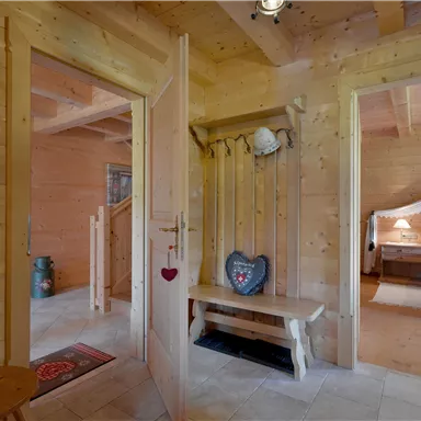 Ein gemütlicher Flur in einem Holzhaus. Die Wände sind aus Holz, und auf der linken Seite sieht man eine Sitzbank mit dekorativen Elementen.