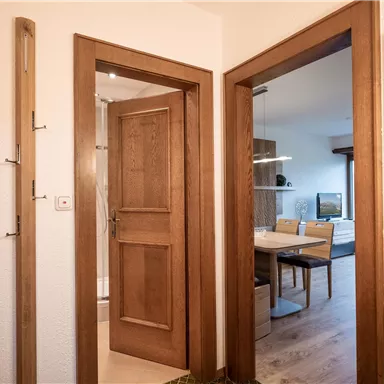 An inviting hallway with wooden doors and a large mirror. In the background, you can see a dining area with a table and a television.