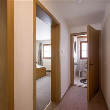 A bright hallway with two open doors. On the left side, there is a bedroom and on the right side, there is a bathroom.