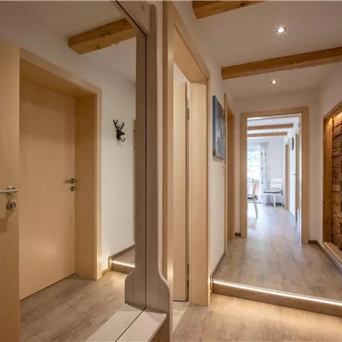 Ein heller Flur mit Holzdetails und modernen Türen. Durch die Fenster ist viel Tageslicht sichtbar.