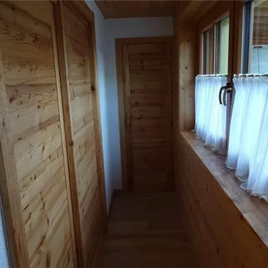 Ein heller Flur mit Holzwänden und einer Fensterbank. Vorhang und Türen aus Holz schaffen eine gemütliche Atmosphäre.