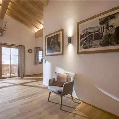 A modern room with a view of the mountains. There is an elegant armchair and two framed pictures on the wall.