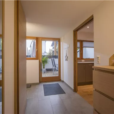 Ein heller Eingangsbereich mit modernen Möbeln. Große Fenster bieten Blick auf eine Terrasse mit Pflanzen.