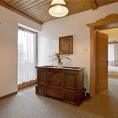 A cozy room with wooden doors and a decorative cabinet. The window provides bright lighting and an inviting atmosphere.