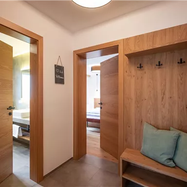 A modern hallway with wood-colored doors and a wardrobe. Two cushions are lying on the bench, and it is bright and inviting.