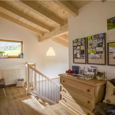 A bright hallway with a wooden ceiling and windows that let in plenty of natural light. Information boards hang on the wall, and a wooden sideboard is in the room.