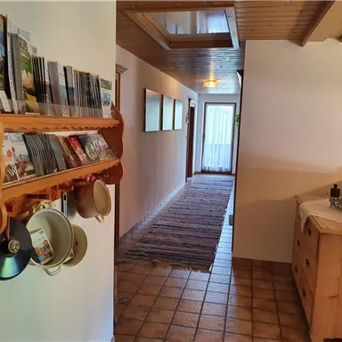 A spacious hallway with wooden shelves for brochures and a dresser. The floor is tiled and a carpet runs along the corridor.