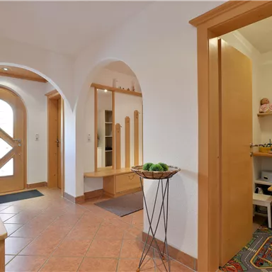 Ein heller Flur mit Holz- und Fliesenboden. Auf der rechten Seite befindet sich ein kleiner Raum mit Spielzeug und einem Tisch für Kinder.