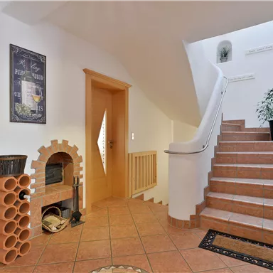 Ein heller Flur mit einer Treppe und einer Pflanze in einem Topf. An der Wand hängt ein dekoratives Bild und ein Kamin aus Terrakotta steht in der Ecke.