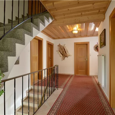 Ein einladender Flur mit einer Treppe und Holzakzenten. Am Boden liegt ein roter Teppich, und die Türen sind aus Holz.
