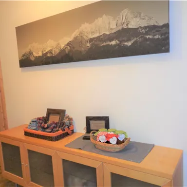 An inviting hallway with a wooden cabinet and a modern wall mural of mountains. Colorful decorations are placed in a bowl on the table.