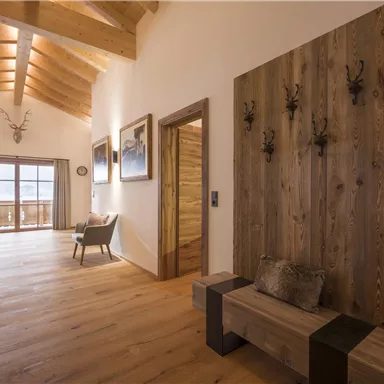 A friendly entrance area with wooden paneling and large windows. The room has a modern, rustic style with wooden flooring and cozy furniture.
