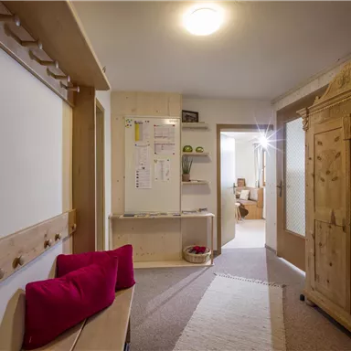 A bright hallway with wooden furniture and a large wardrobe. Notes hang on the wall and there is a bench with red cushions.