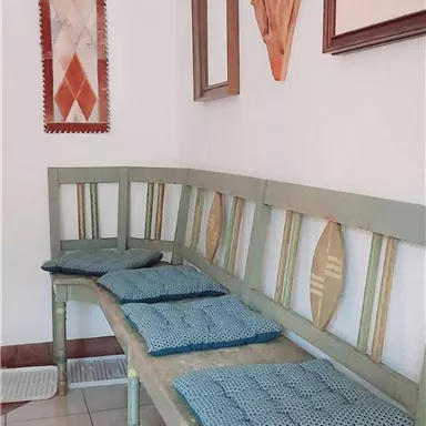 A cozy bench with blue cushions is against the wall. Decorative artworks and a mirror are mounted on the wall.