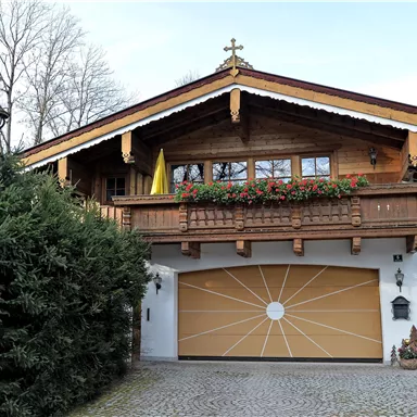 A traditional chalet with a balcony and flower boxes. The garage has a striking, round design.