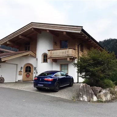 Ein modernes Haus im alpinen Stil mit Holzverkleidung. Vor dem Haus steht ein blauer Sportwagen auf der Auffahrt.