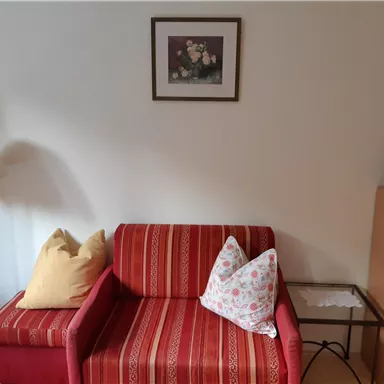A cozy living area with a red striped sofa and two cushions. Next to the sofa is a lamp and a small table with a coffee pot.