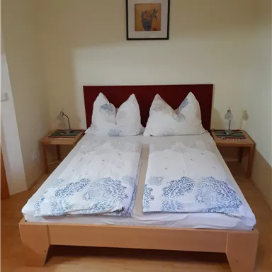 A cozy bedroom with a double bed and two nightstands. The walls are light, and a picture hangs above the bed.