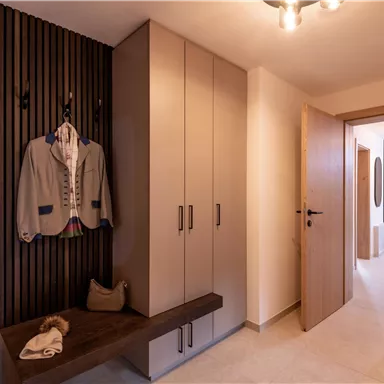 A modern entrance area with a wardrobe and a wooden bench. A jacket hangs on the wall and the room is bright and inviting.