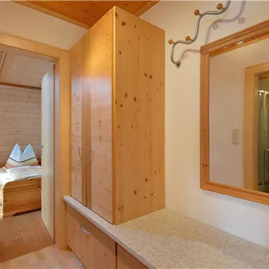 Ein heller Flur mit Holzschränken und einem Spiegel. Im Hintergrund ist ein gemütliches Schlafzimmer sichtbar.