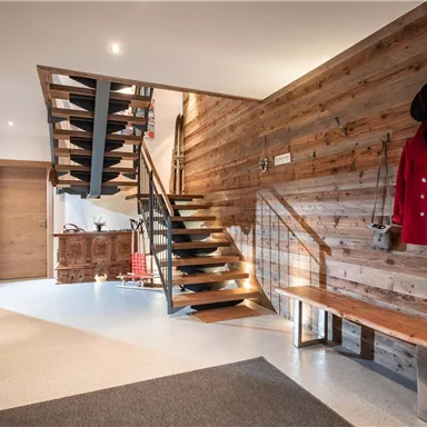 Ein modernes Eingangsbereich mit einer eleganten Holztreppe. Die Wände sind aus Holz und es gibt Sitzbänke sowie einen Spiegel.