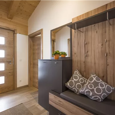 Ein modernes Entré mit Holzwänden und einer stilvollen Garderobe. Eine gemütliche Sitzgelegenheit mit dekorativen Kissen lädt zum Verweilen ein.
